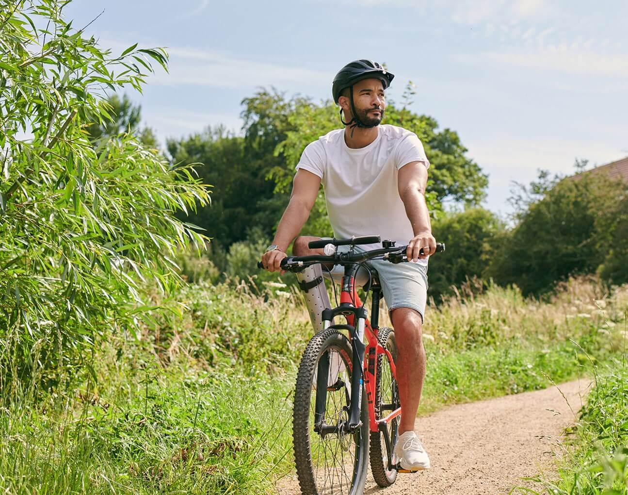 cyclist wearing helmet dressed in shorts and tshirt on country lane surrounded by trees and grass
