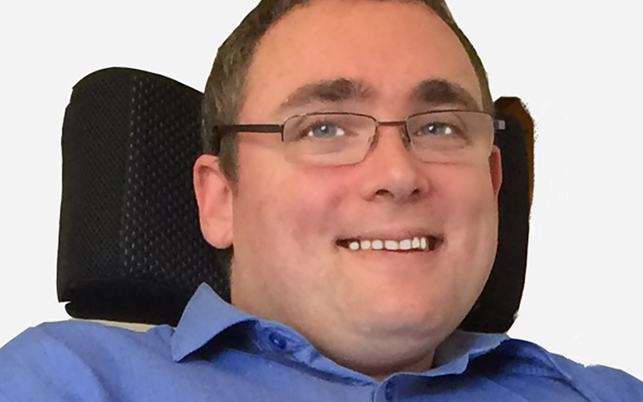 smiling headshot photo of ncat Board member Damian Bridgeman, wearing blue shirt and glasses sitting in a chair