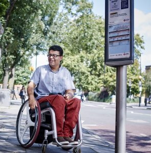 man using wheelchair waiting at bus stop on a sunny day