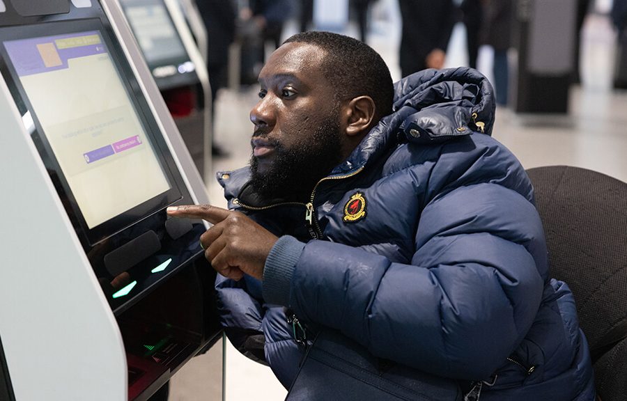 male wheelchair user is pressing buttons on a ticket screen at Heathrow airport