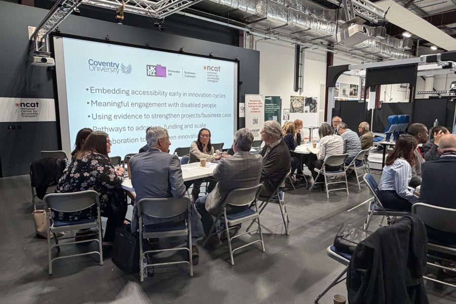 Groups of professionals seated at round tables in a modern workshop space, taking part in discussions on accessible transport innovation.