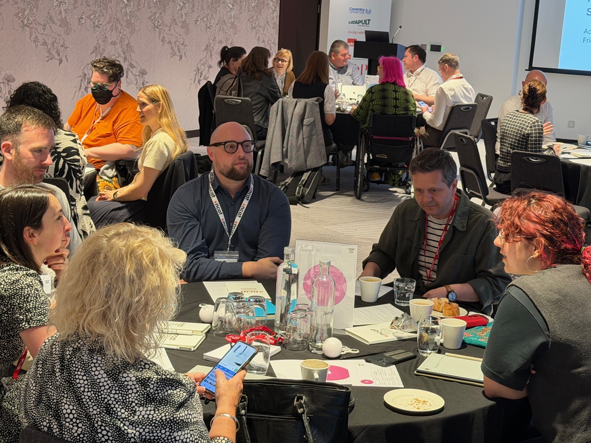 Several groups of people sitting at round tables in a meeting room having discussions.